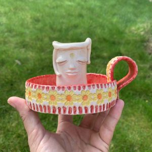 handmade ceramic whimsical candle holder, with a kind face and red Mediterranean vibe base. It does have a handle
