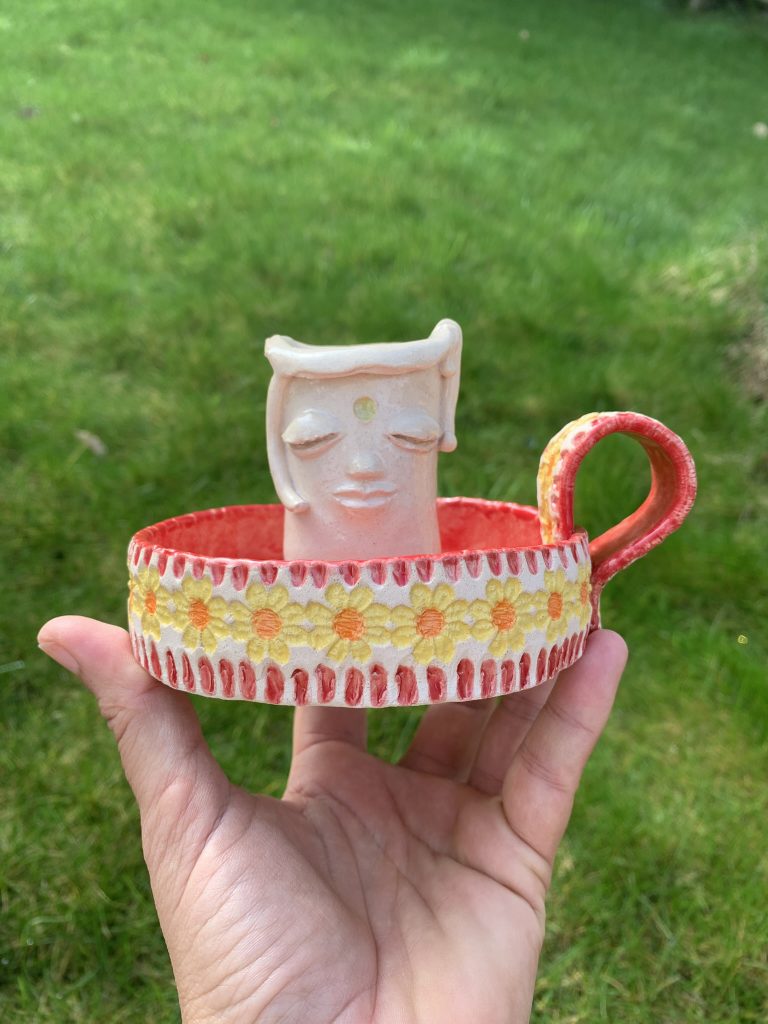 handmade ceramic whimsical candle holder, with a kind face and red Mediterranean vibe base. It does have a handle