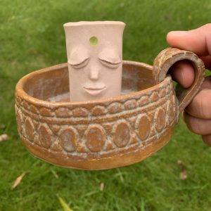 handmade whimsical ceramic candle holder with handle. It has a kind face and patterned texture in the base