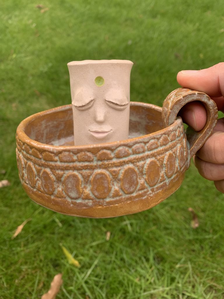 handmade whimsical ceramic candle holder with handle. It has a kind face and patterned texture in the base