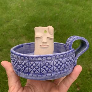 ceramic whimsical candle holder with a kind face and Mediterranean vibes textured base. It also has a handle